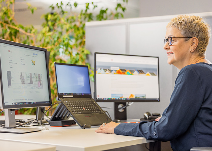 reife Frau sitzt i einem Büro und schaut auf mehrere Bildschirme