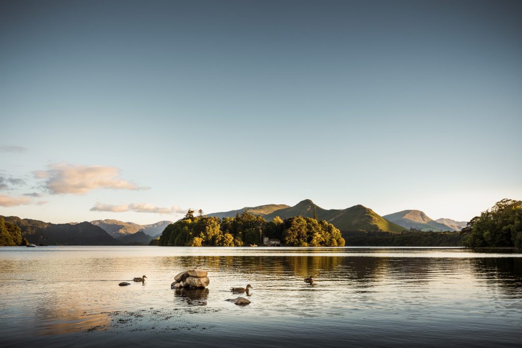 Keswick ist eine wunderschöne Stadt im englischen Lake District, wo die üppigen grünen Hügel auf den ruhigen See Derwentwater treffen. Die Aufnahme entstand im Sommer am späten Nachmittag. Im Hintergrund ist der Cat Bells Fell zu sehen.