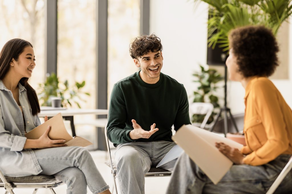 Konzept der Teamarbeit. International befreundete Studenten, die auf Stühlen im Coworking Space sitzen und über ihr gemeinsames Bildungsprojekt diskutieren