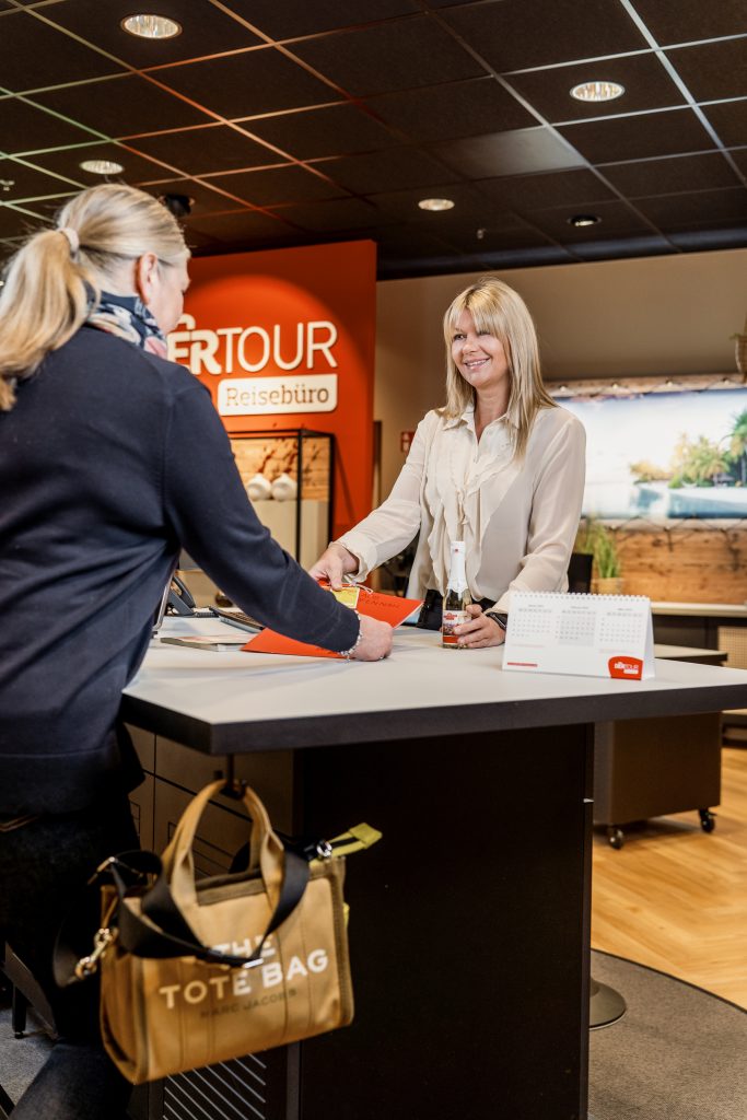 Frau in einem Reisebüro übergibt einer anderen Frau Reiseunterlagen