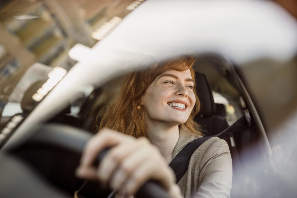 Schöne junge Frau fährt ihr neues Auto bei Sonnenuntergang. Frau im Auto. Close up Porträt der angenehm aussehende Frau mit fröhlich positiven Ausdruck, Frau in Freizeitkleidung fahren ein Auto