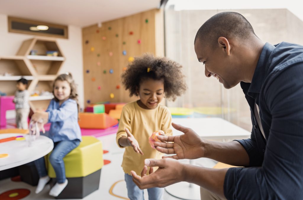 Glückliche Grundschüler, die in der Schule mit Schleim spielen und ihn der Lehrerin zeigen - Bildungskonzepte