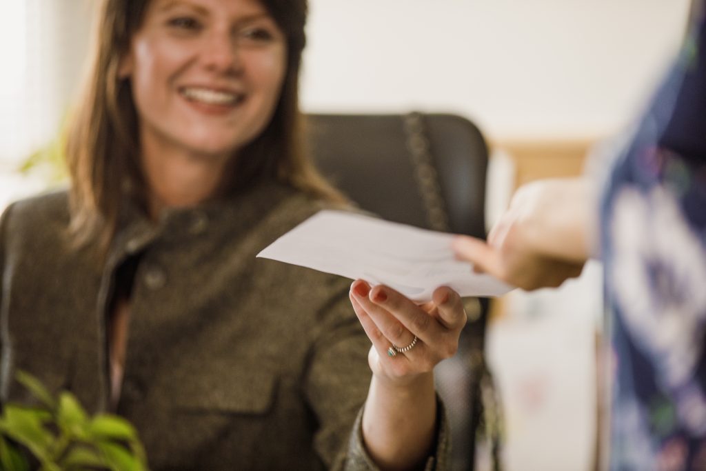 Selektive Schärfeeinstellung einer lächelnden Geschäftsfrau im mittleren Erwachsenenalter, die an ihrem Schreibtisch sitzt und ihrer Kollegin ein Dokument überreicht