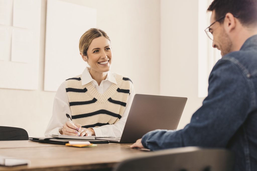 Weibliche Personalchefin im Gespräch mit einem Bewerber in ihrem Büro. Glückliche junge Geschäftsfrau bei einem Treffen mit einem Bewerber in der engeren Auswahl in ihrem Büro.