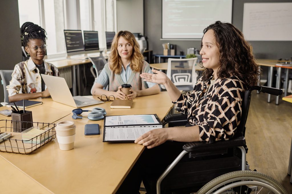 Büroangestellte im Rollstuhl bespricht Papiere mit Infografiken mit gemischtrassigen Kollegen am Schreibtisch