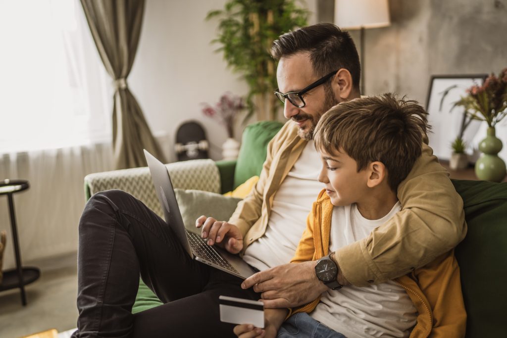 Vater und Sohn kaufen online mit Kreditkarte auf Laptop zu Hause
