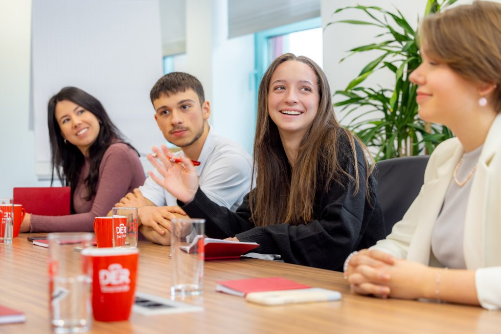 vier junge Menschen sitzen in einem Büro in einer Reihe und besprechen etwas