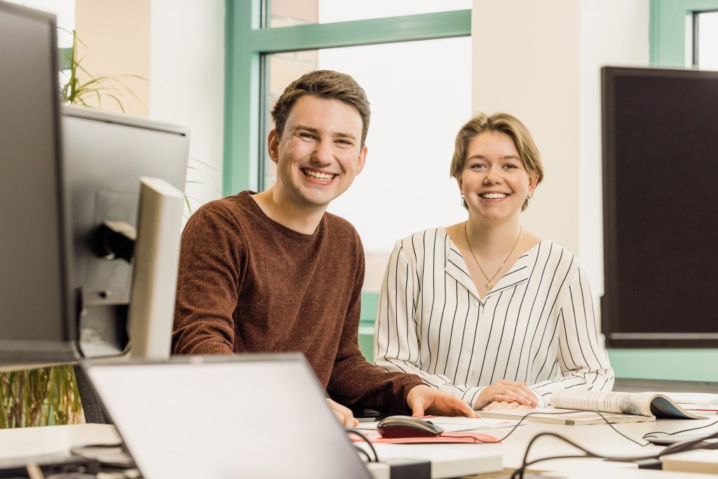 junge Menschen sitzen in einem Büro und lachen in die Kamera