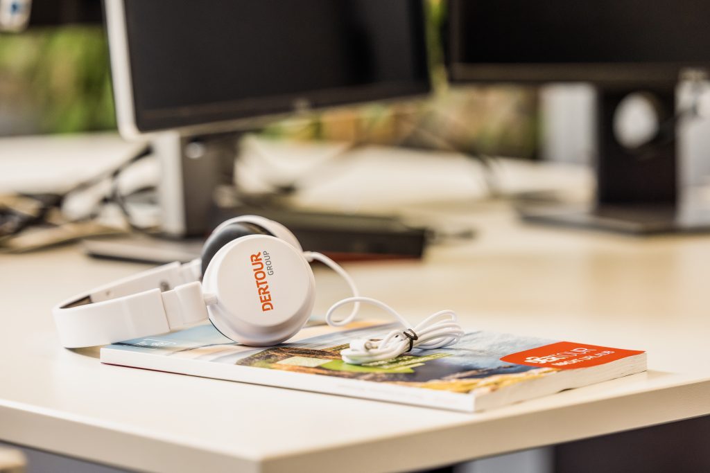 weiße Kopfhörer mit DERTOUR Group Logo liegen auf einem Katalog auf einem Schreibtisch