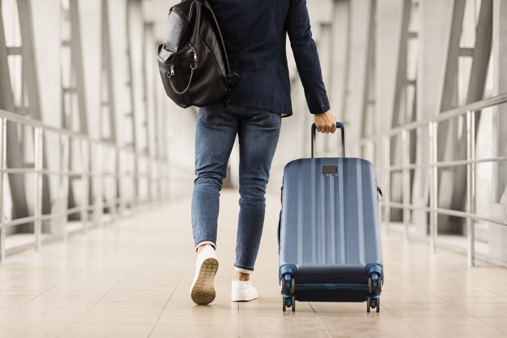 Mitarbeiter in Jeans und Blazer zieht einen blauen Trolley-Koffer in einem modernen Flughafen-Terminal